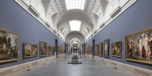 Museum wing with a long hallway with paintings on purple walls and a white with skylight arched ceiling